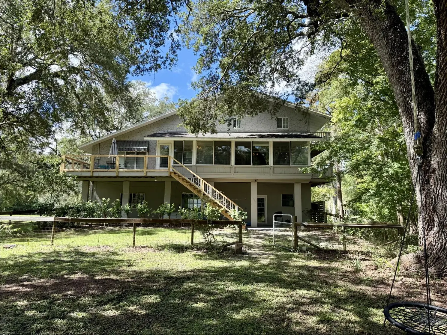 The elevated house seen from the back lawn, framed by ancient oaks
