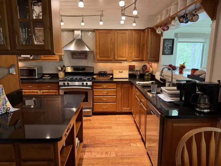 The full kitchen with gas range, stone counters and wood cabinetry