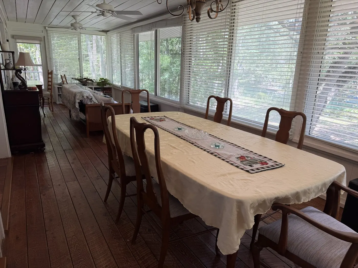The Florida room's long dining table running beside a wall of windows into the trees